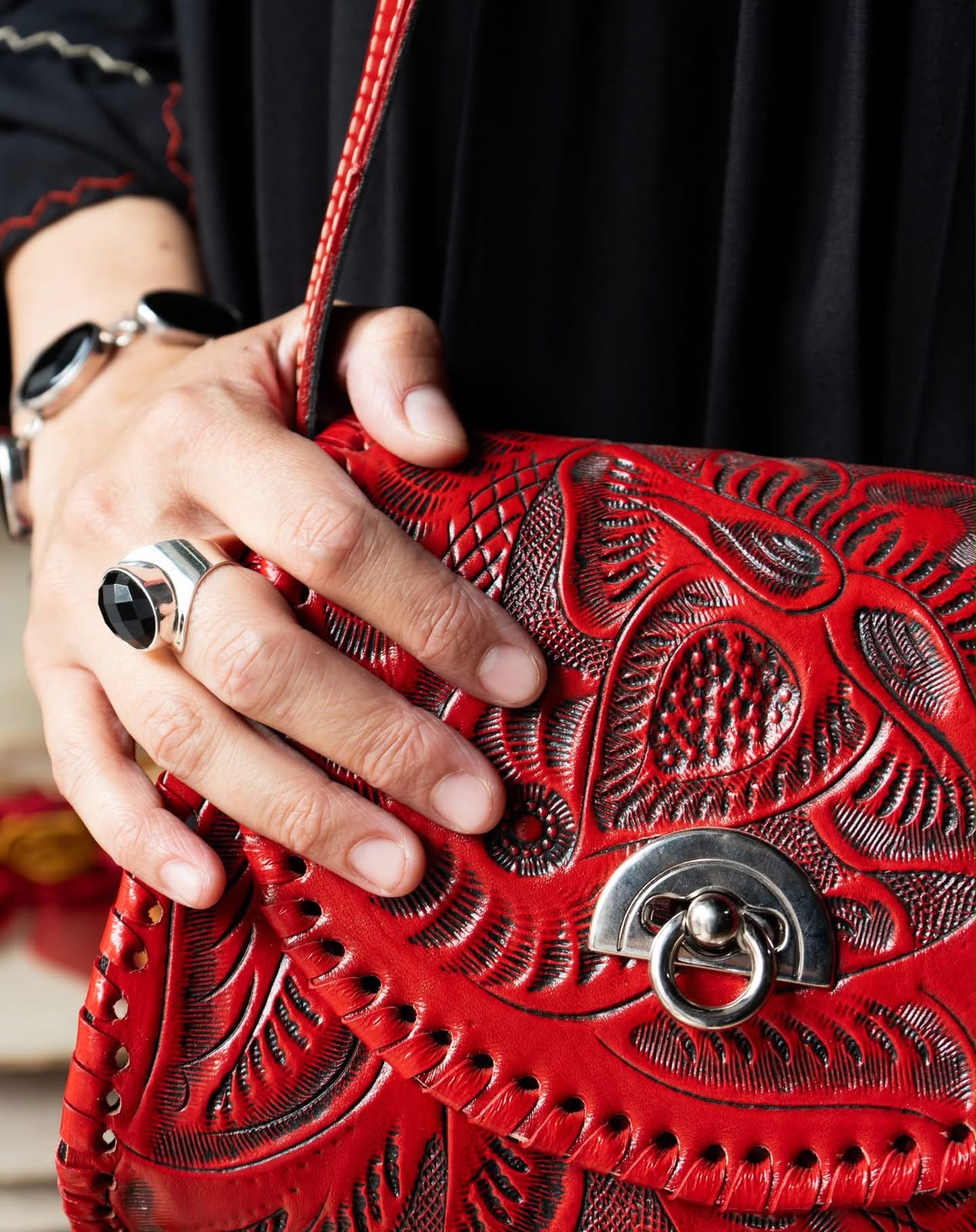 Bolso artesanal de cuero rojo grabado, acompañado de joyería de plata y piedra negra